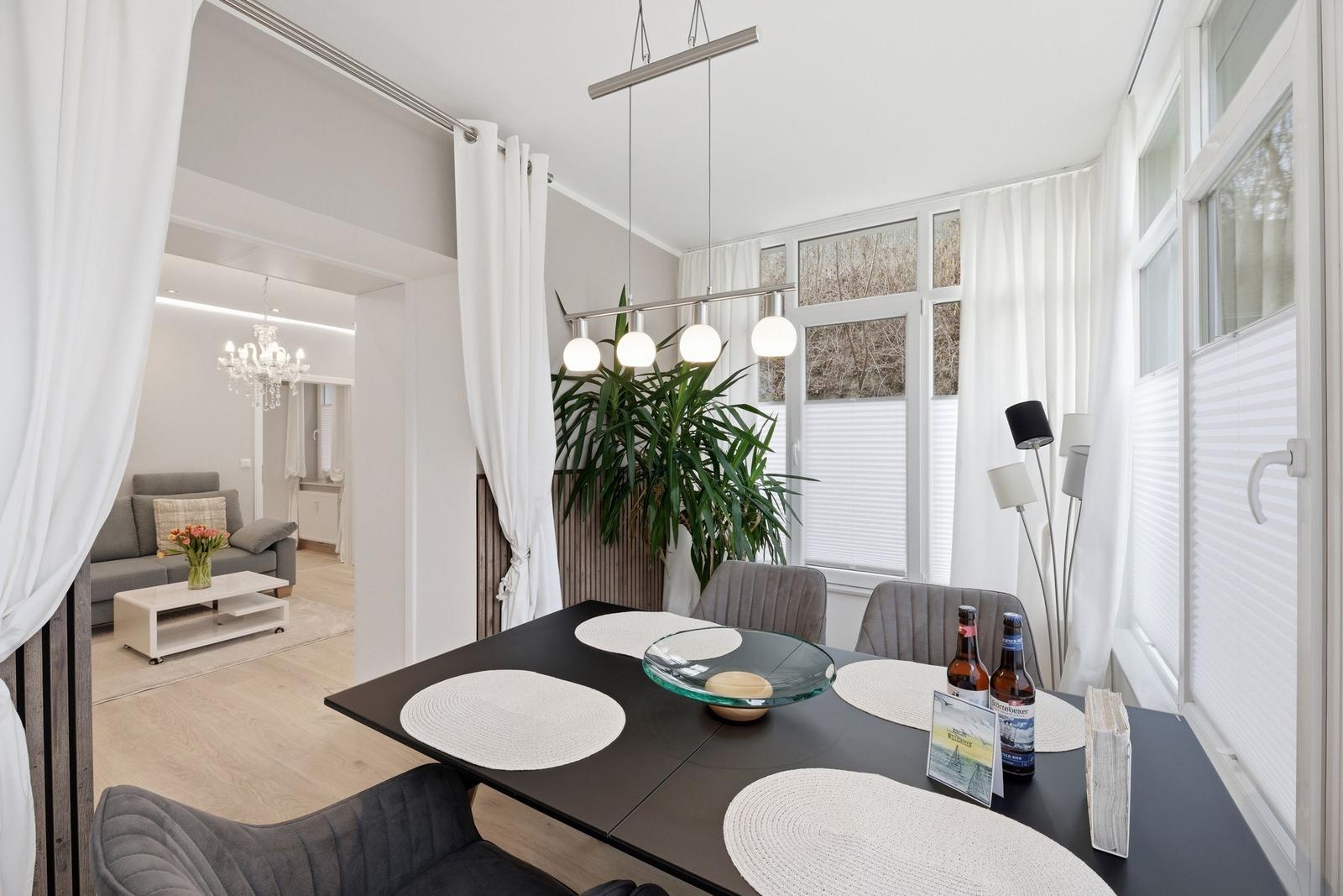 Esstisch mit Stühlen und Fensterblick. Wohnzimmer im Hintergrund.