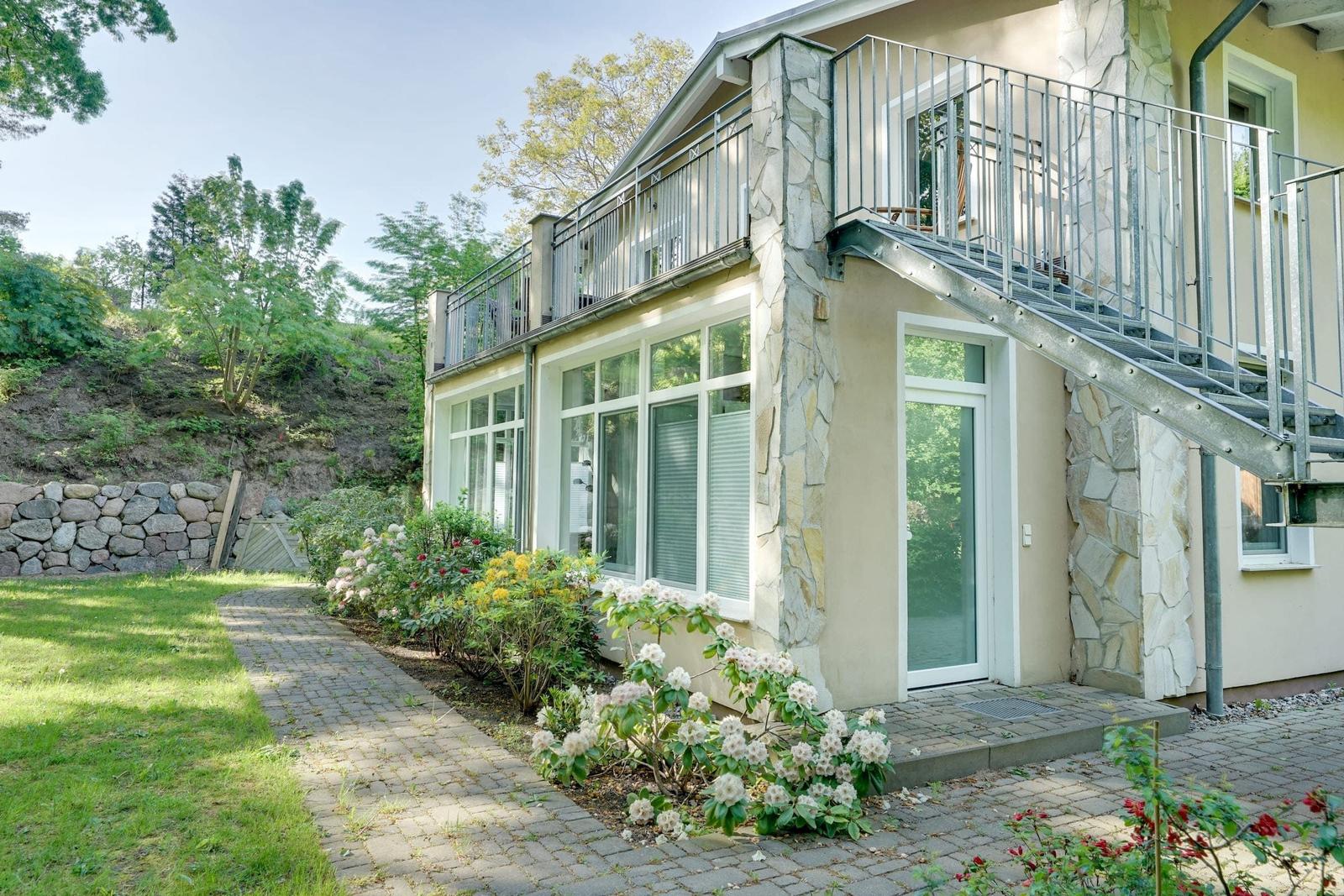 Haus mit Balkon, Steintreppe und Blumenbeete im Garten