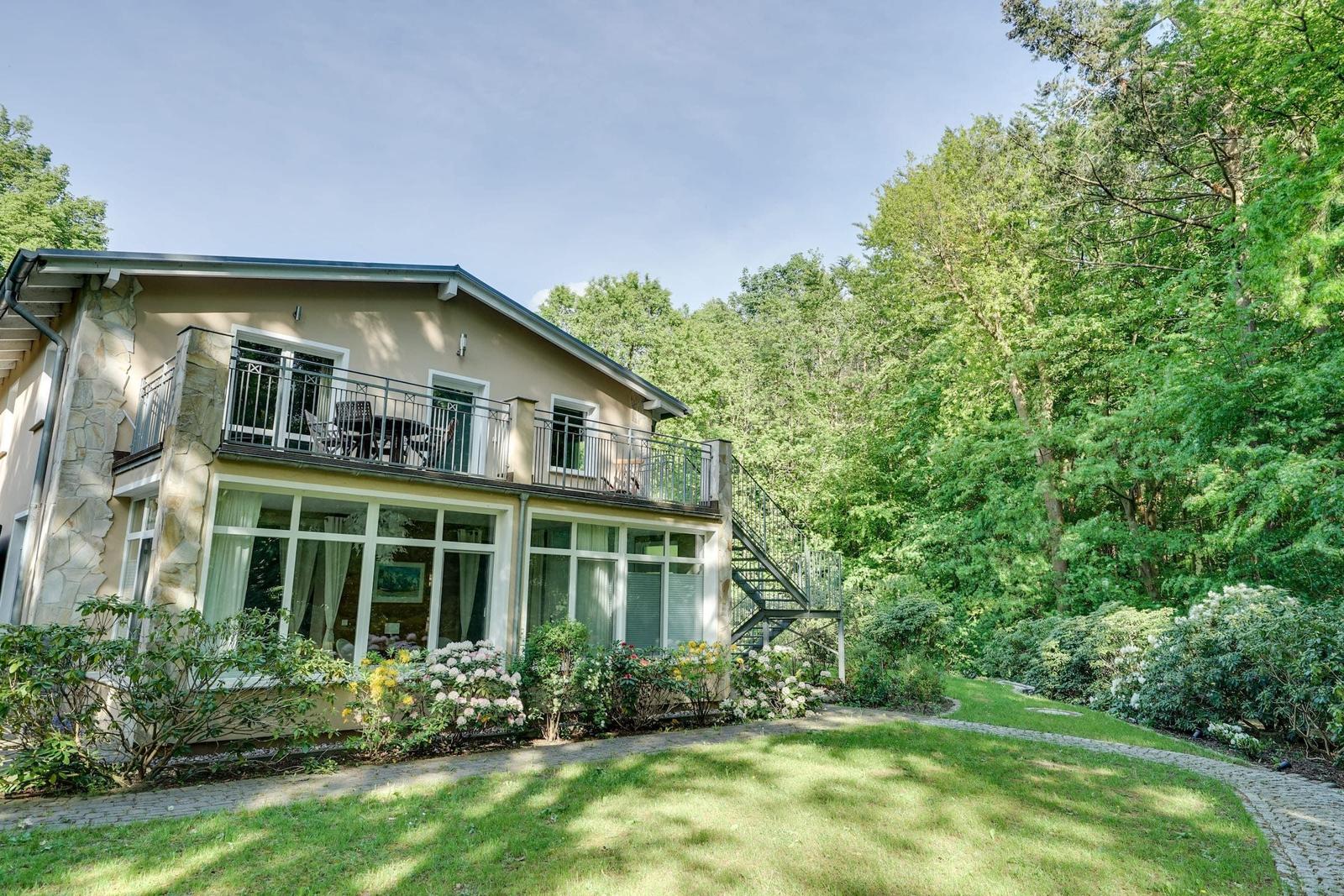 Haus mit Balkon, Garten und Wald im Hintergrund.