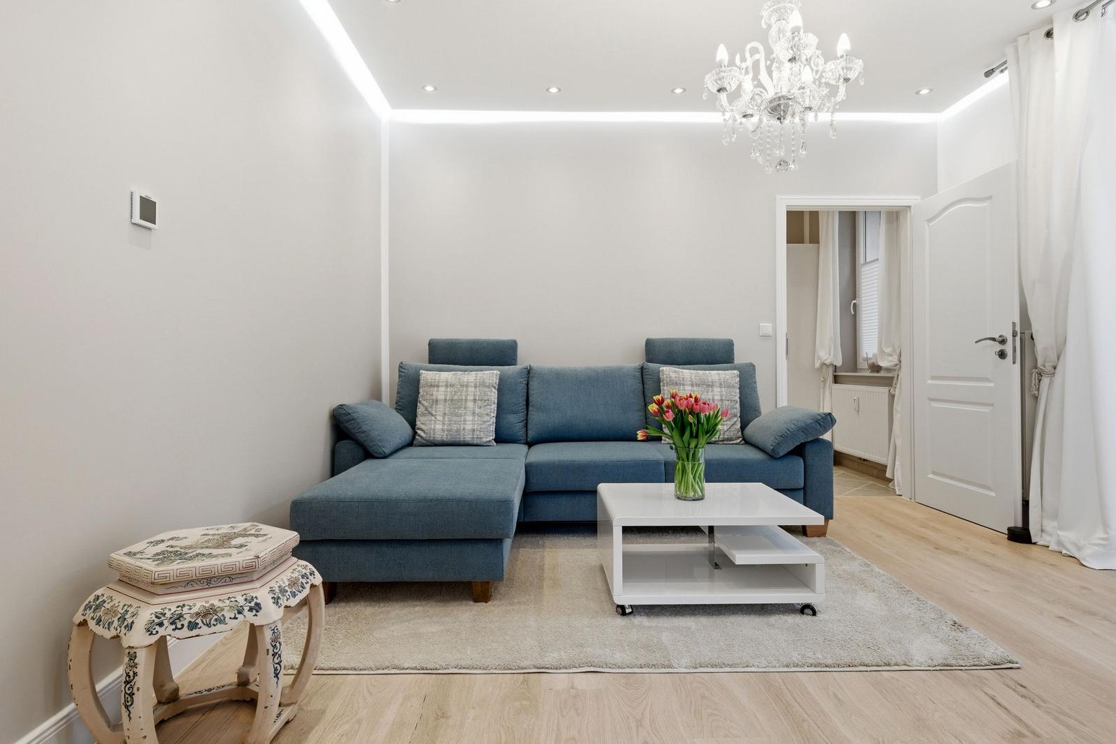 Ein Wohnzimmer mit blauem Sofa, weißem Couchtisch und Kronleuchter.