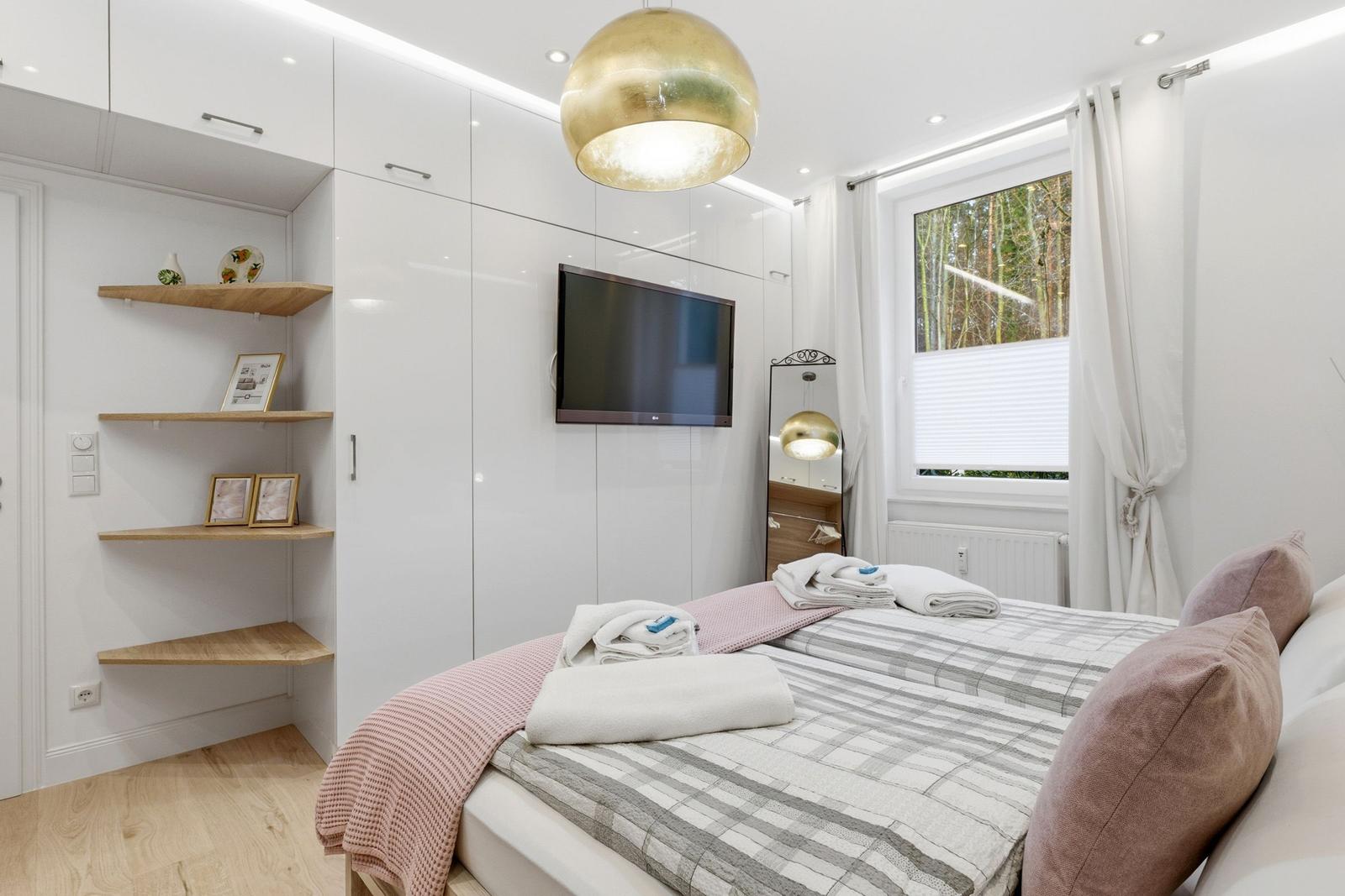 Schlafzimmer mit Bett, TV und Fenster zum Wald