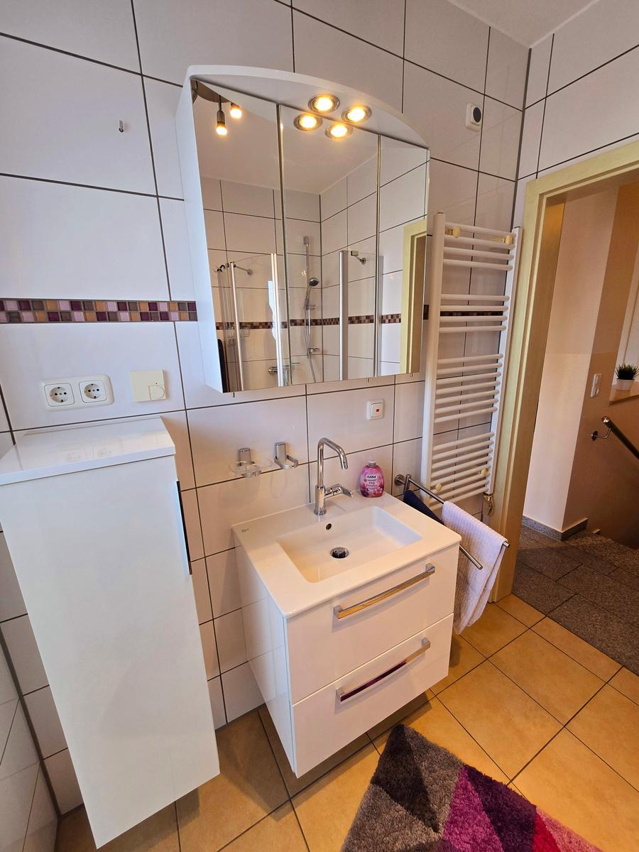 Helles Badezimmer mit Waschplatz, Dusche und ausreichend Stauraum.