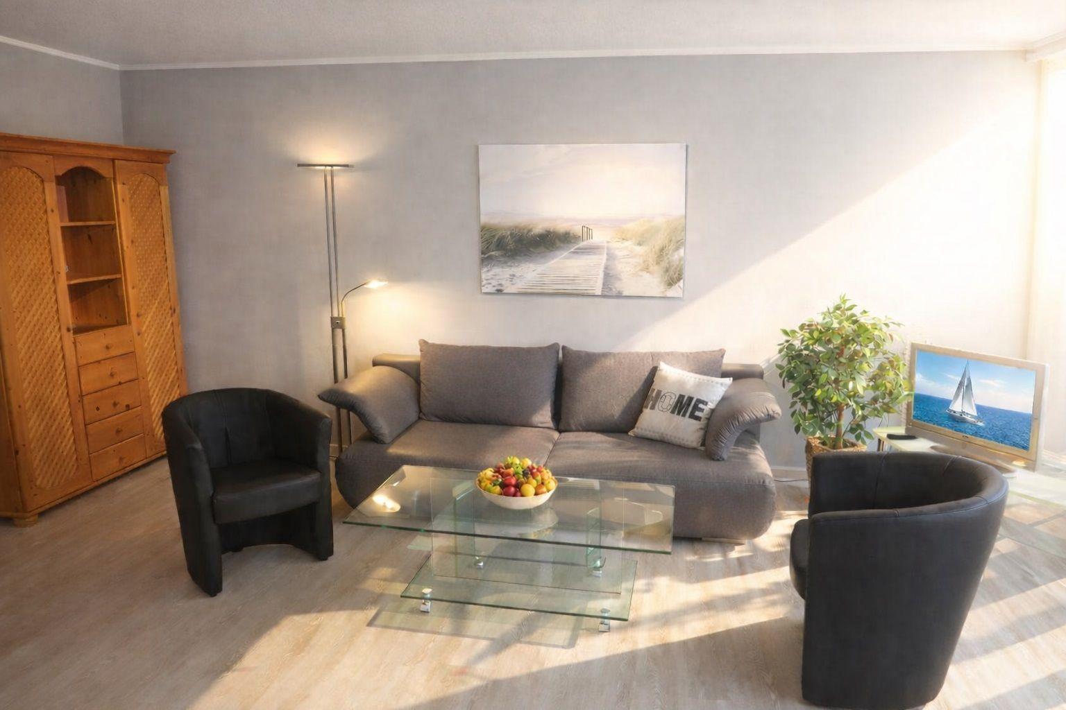 Wohnzimmer mit grauem Sofa, zwei schwarzen Sesseln und Glas-Tisch. Wandbild und Pflanze sichtbar.