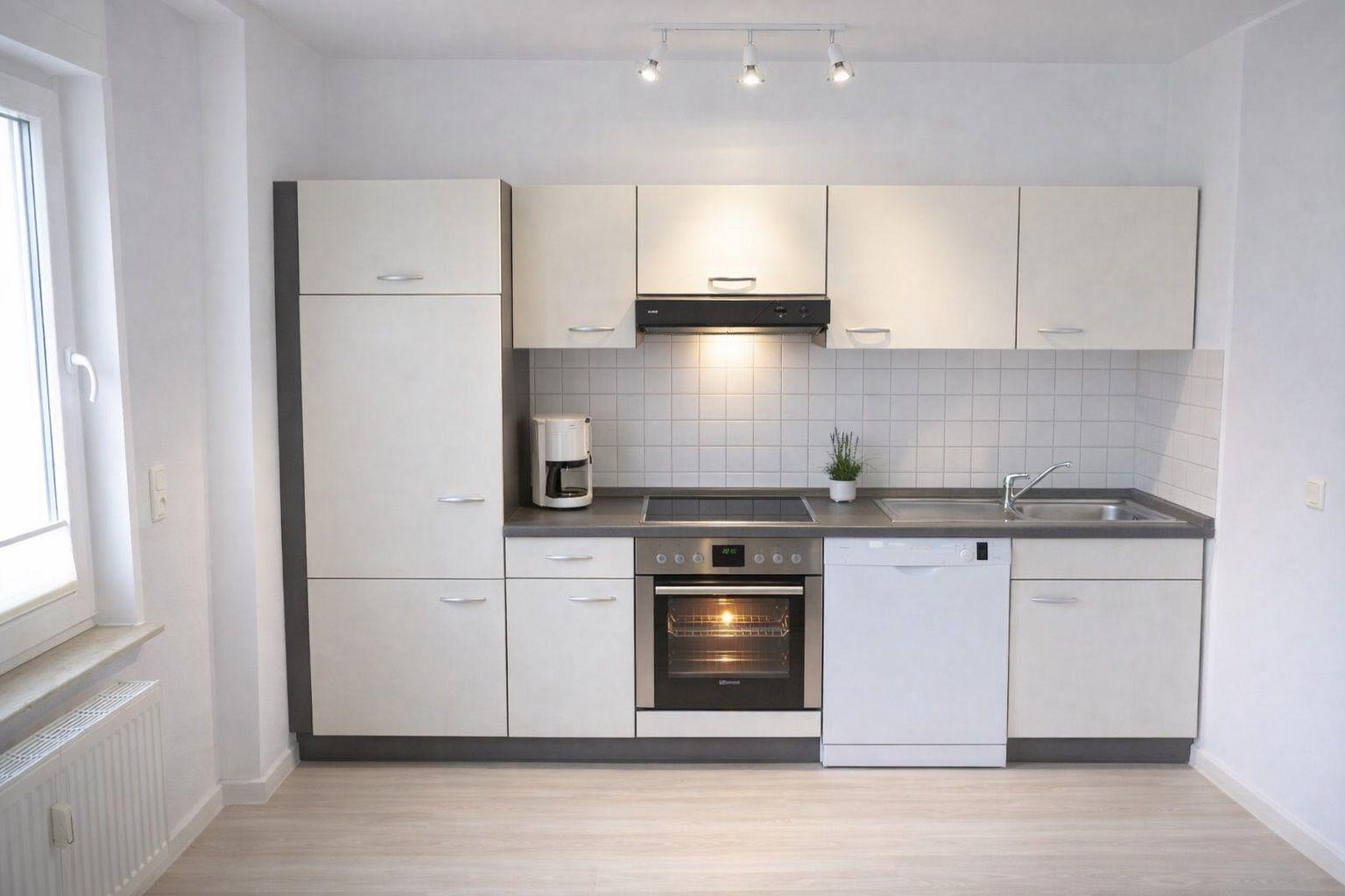 Moderne Küche mit weißen Schränken, Edelstahlspüle und integriertem Backofen.