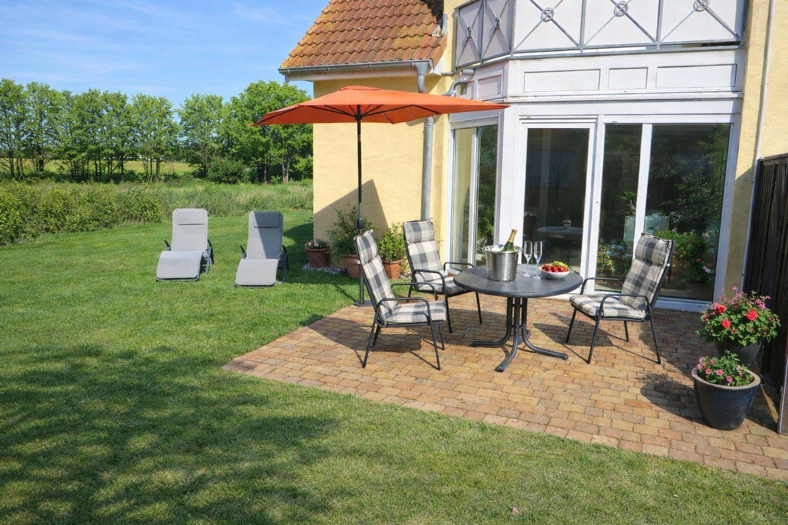Terrasse mit Tisch, Stühlen und Sonnenschirm. Grasfläche und Blick auf Wiese.