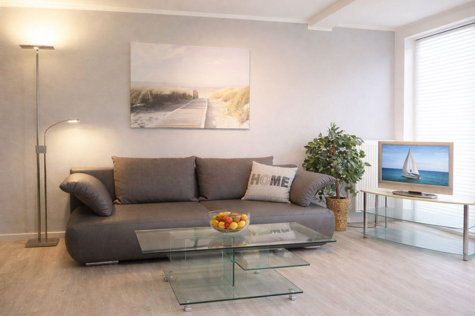 Ein Wohnzimmer mit grauem Sofa, Glas-Tisch und Fernseher.