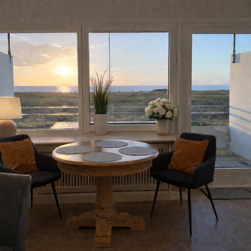 Rundtisch mit Stühlen vor Fenster mit Meerblick bei Sonnenuntergang.