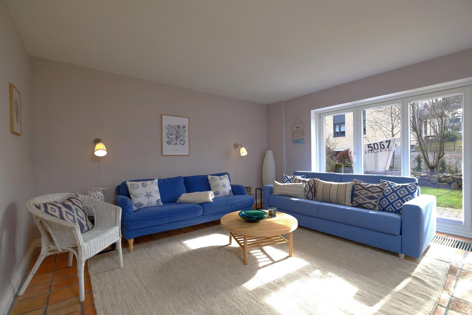 Zwei blaue Sofas, ein runder Tisch und ein weißer Stuhl im Wohnzimmer mit Blick auf den Garten.