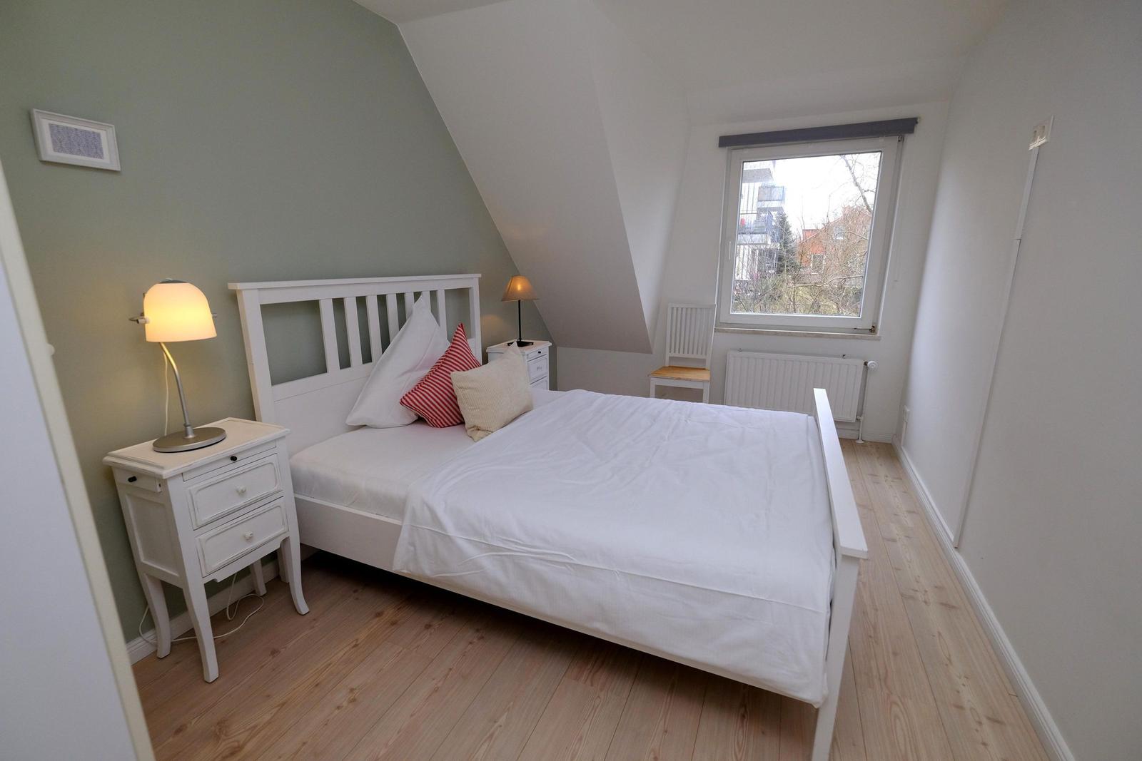 Schlafzimmer mit weißem Bett, Nachttisch und Fenster.
