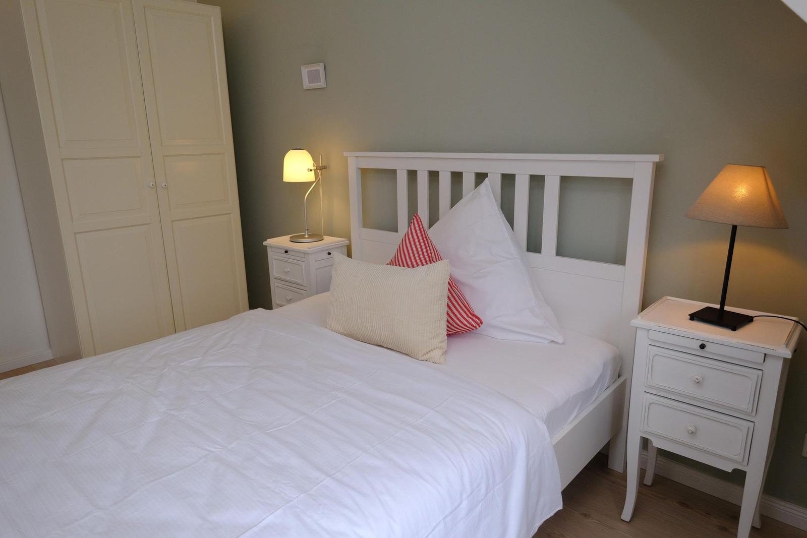 Schlafzimmer mit weißem Bett, Nachttischen und Kleiderschrank.
