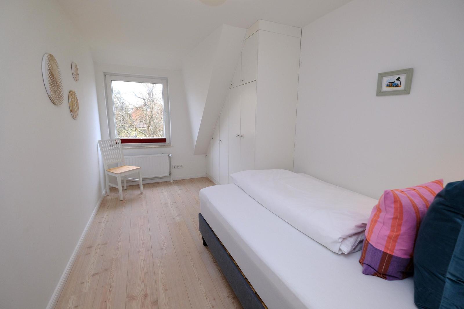 Schlafzimmer mit Bett, Schrank und Fenster. Holzboden und Wanddekoration.