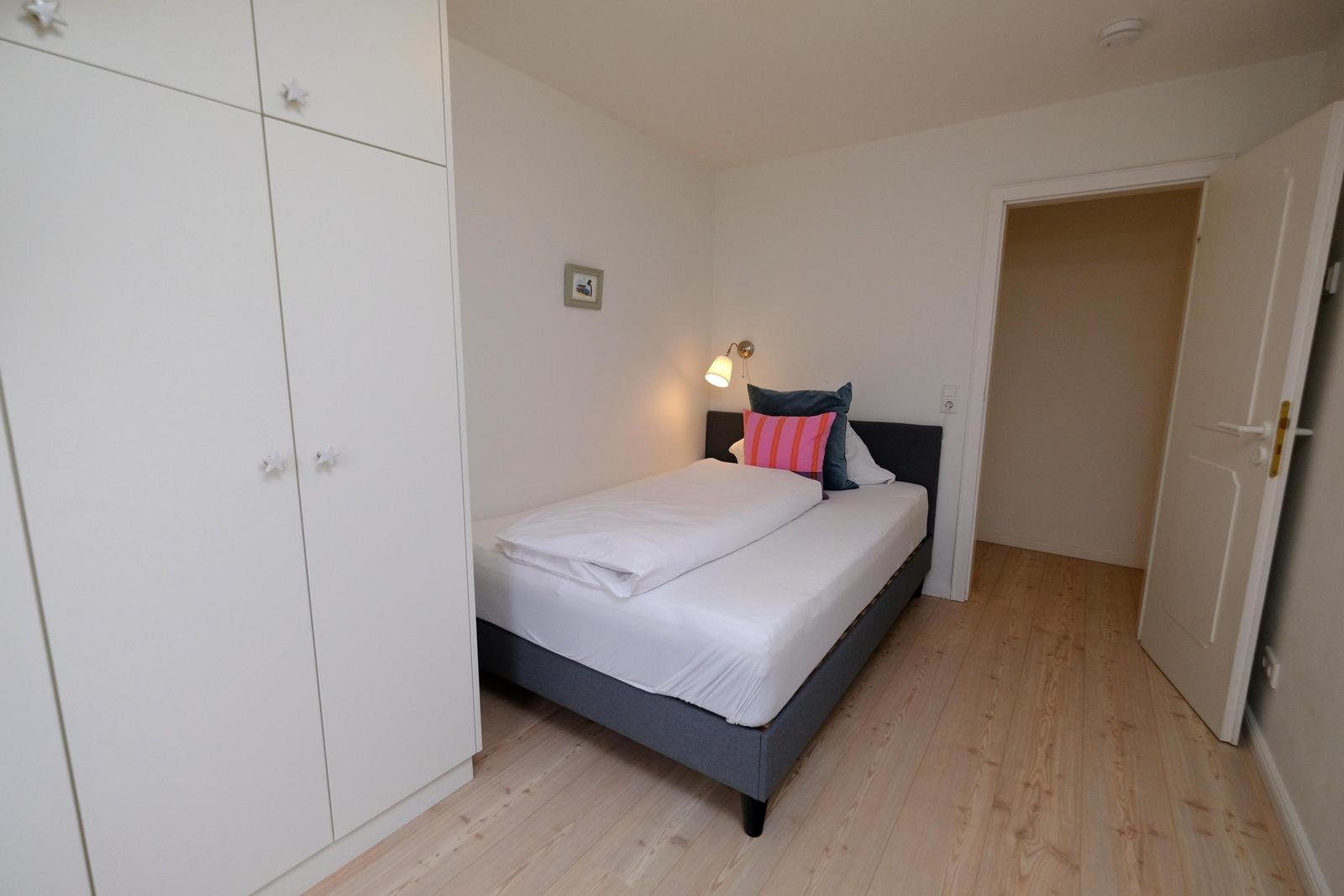 Schlafzimmer mit Bett, Kleiderschrank und Holzboden.