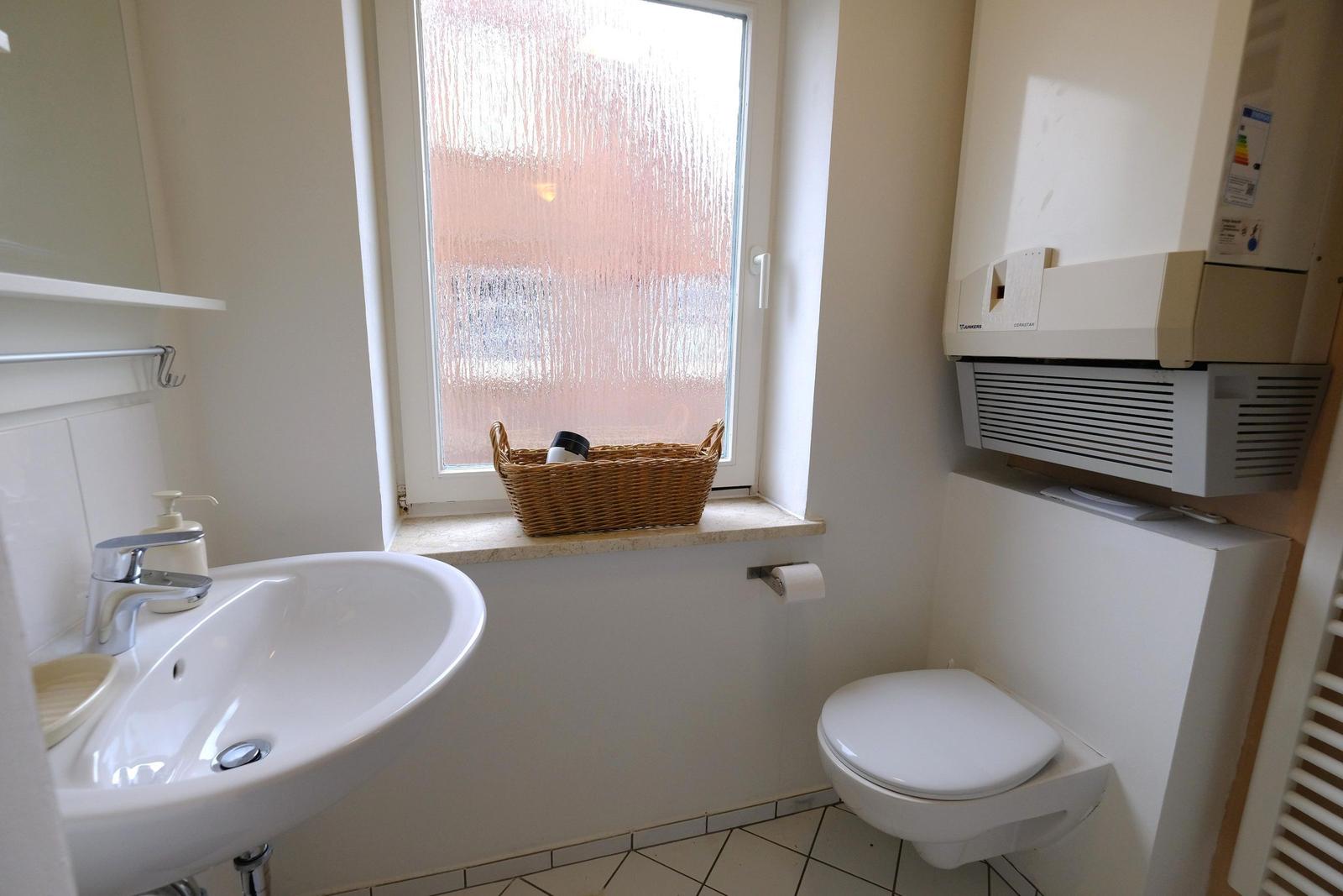 Badezimmer mit Waschbecken, Toilette und Fenster mit Korb.