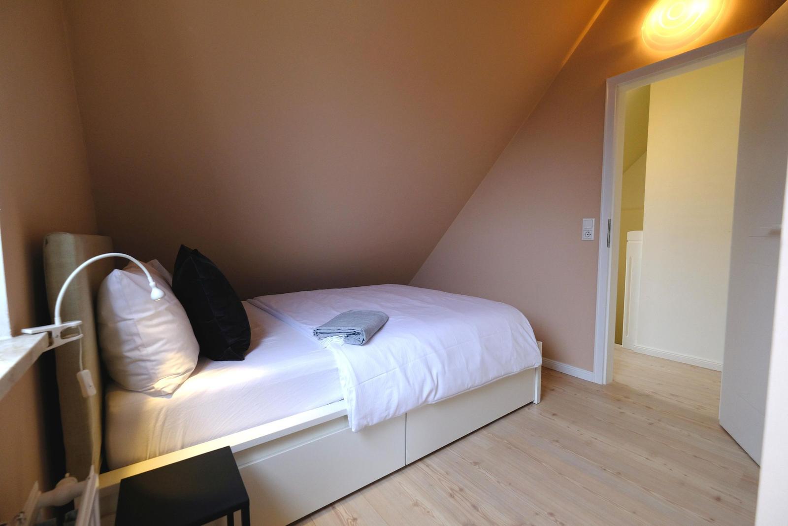 Schlafzimmer mit Bett, Kissen und Holzboden unter schräger Decke.