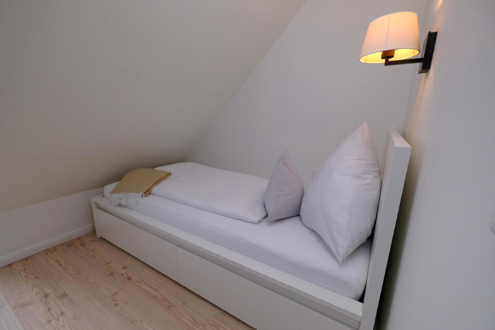 Schlafzimmer mit Dachschräge, weißem Bett und Wandlampe.