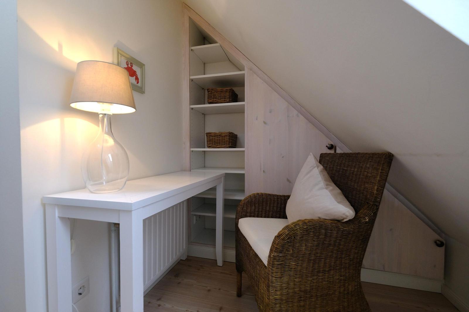 Eckzimmer mit Schreibtisch, Stuhl und Regal unter Dachschräge.