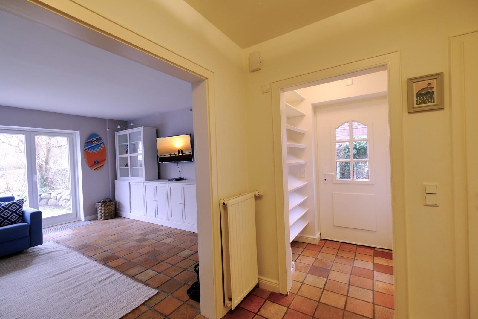 Haus mit Wohnbereich, TV und Terrasse. Tür führt zum Flur mit Regal.
