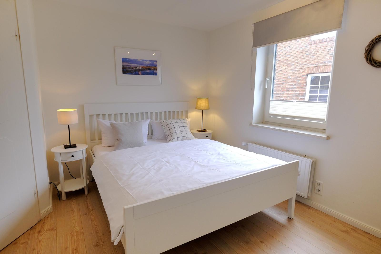 Schlafzimmer mit weißem Bett, zwei Nachttischen und Fenster.