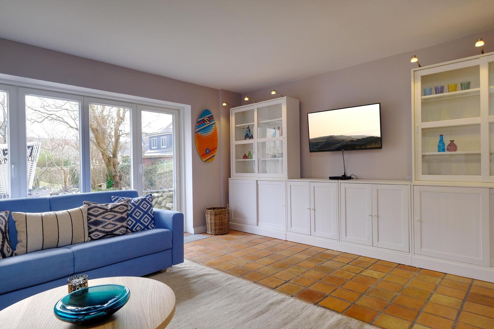 Ein Wohnzimmer mit blauem Sofa, TV und weißen Schränken.