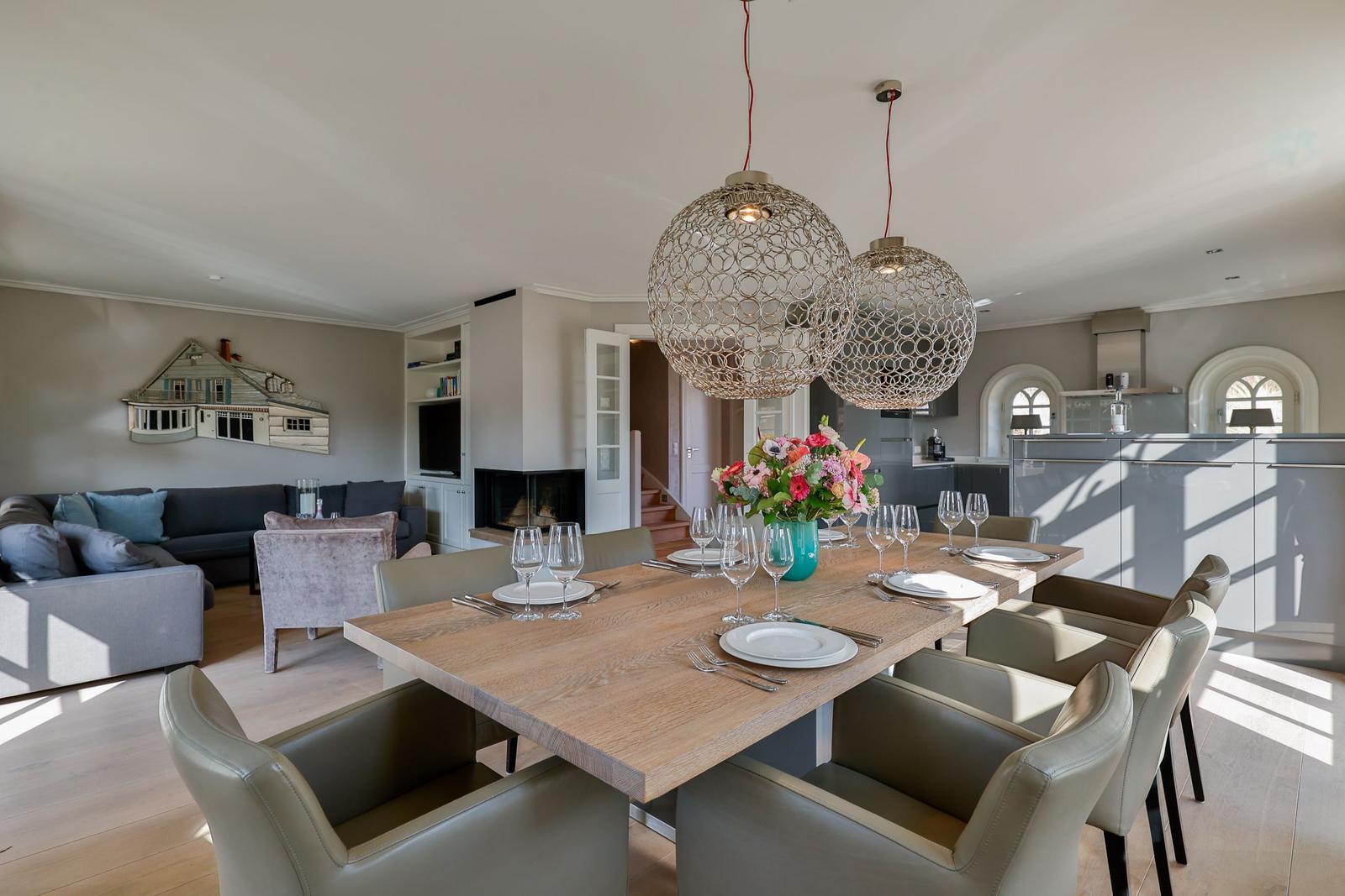 Essbereich mit Holztisch und Stühlen, moderne Pendelleuchten, Küche im Hintergrund.