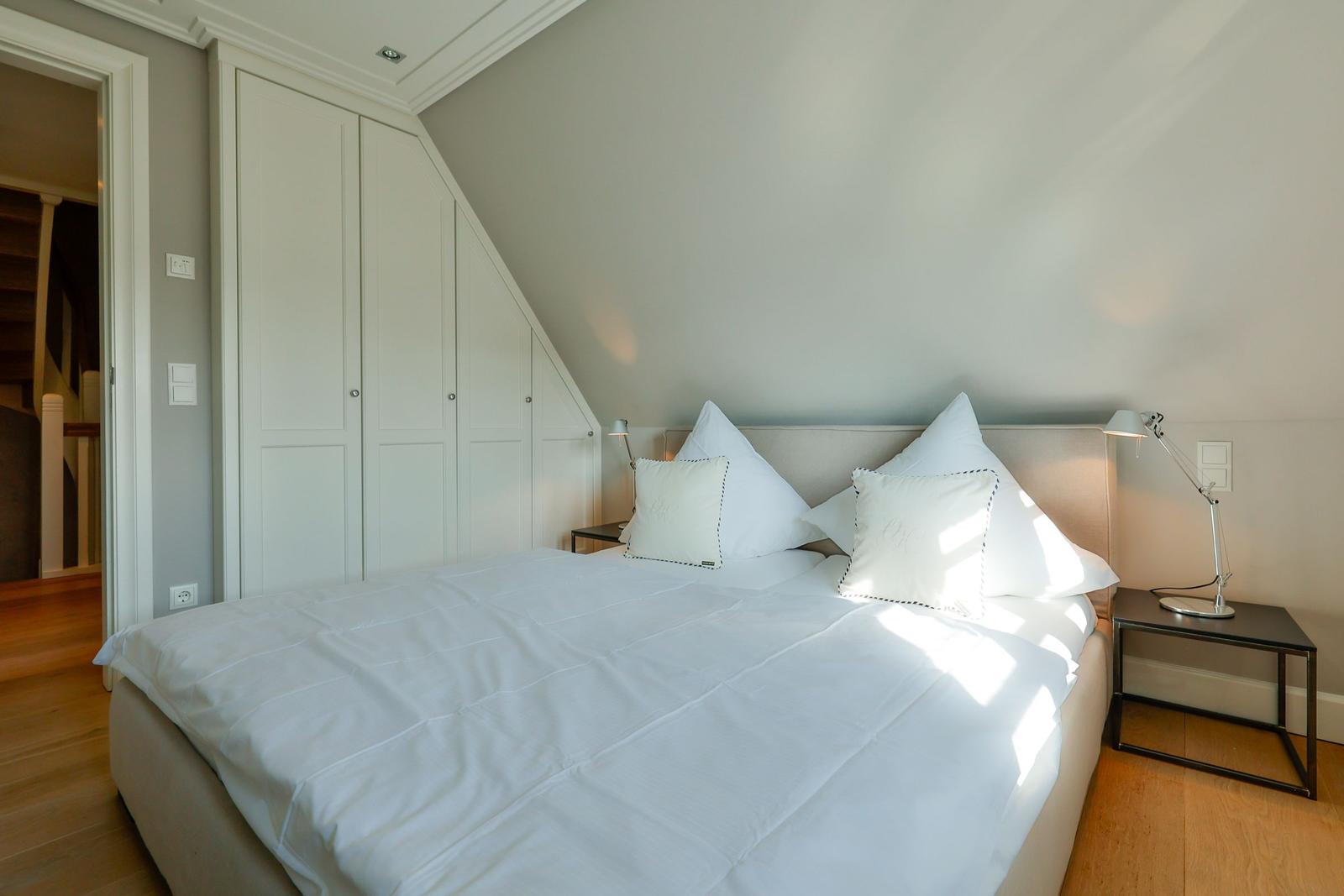 Schlafzimmer mit weißem Bett, Nachttischen und Schrank unter Dachschrägen.
