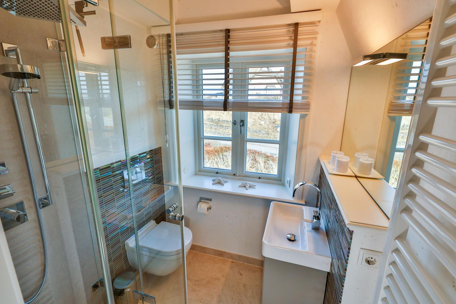 Badezimmer mit Dusche, Toilette und Waschbecken. Fenster mit Jalousie und Handtuchwärmer.