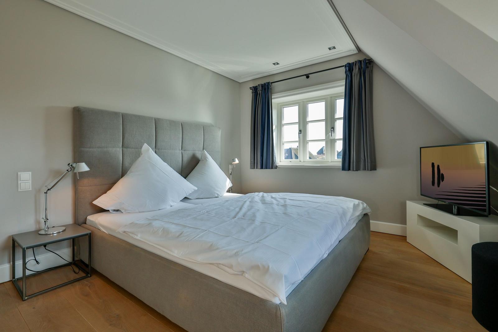 Schlafzimmer mit Bett, Fenster, TV und Nachttisch.