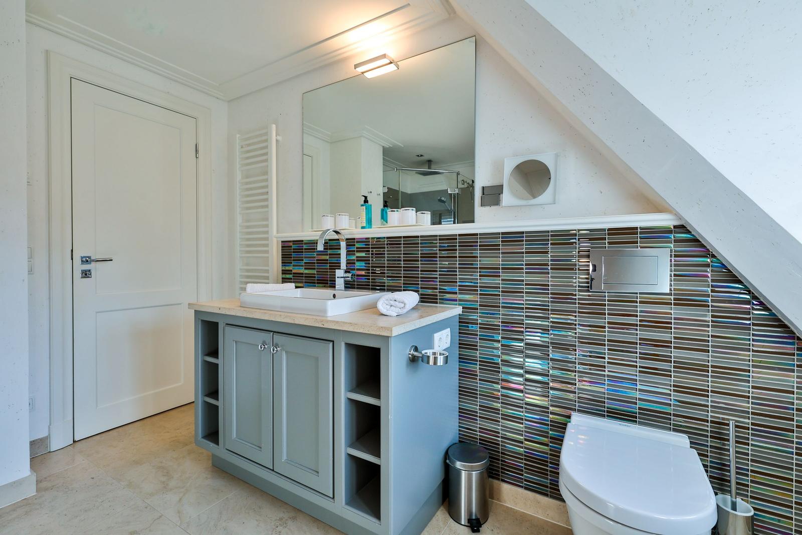 Badezimmer mit Waschbecken, Spiegel und Toilette. Wandverkleidung mit bunten Fliesen.