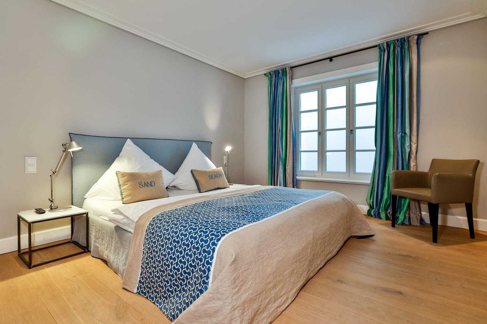 Schlafzimmer mit Bett, Fenster, Vorhängen und Sessel.
