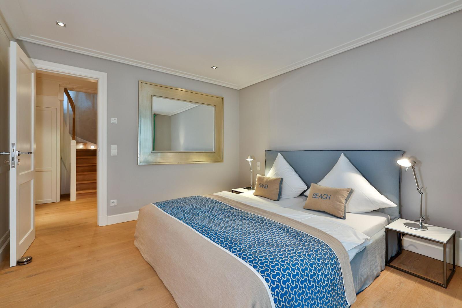 Schlafzimmer mit Bett, Spiegel und Nachttisch. Tür führt zu Treppe.