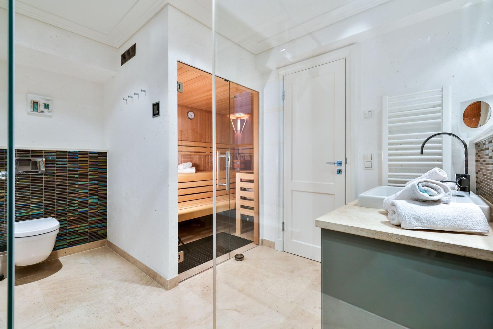 Dusche, Toilette und Sauna in einem Raum mit Glaswand und Holzbank.