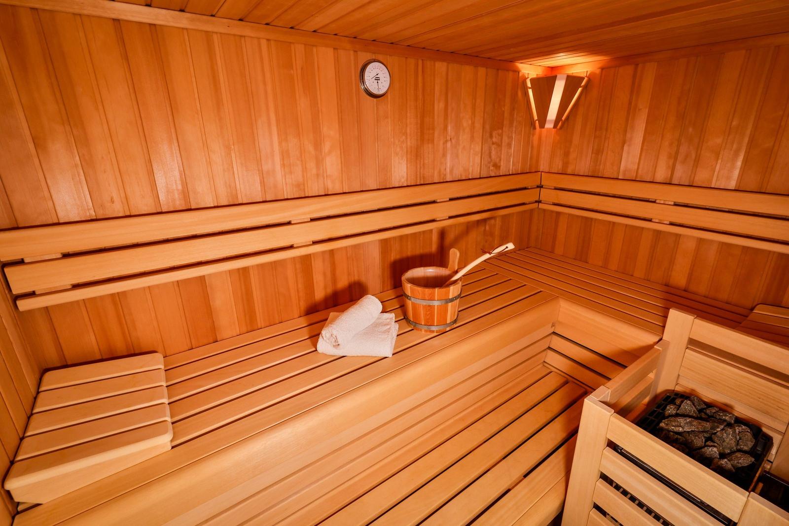 Holzsauna mit Sitzbänken, Thermometer und Holzwaschbecken.