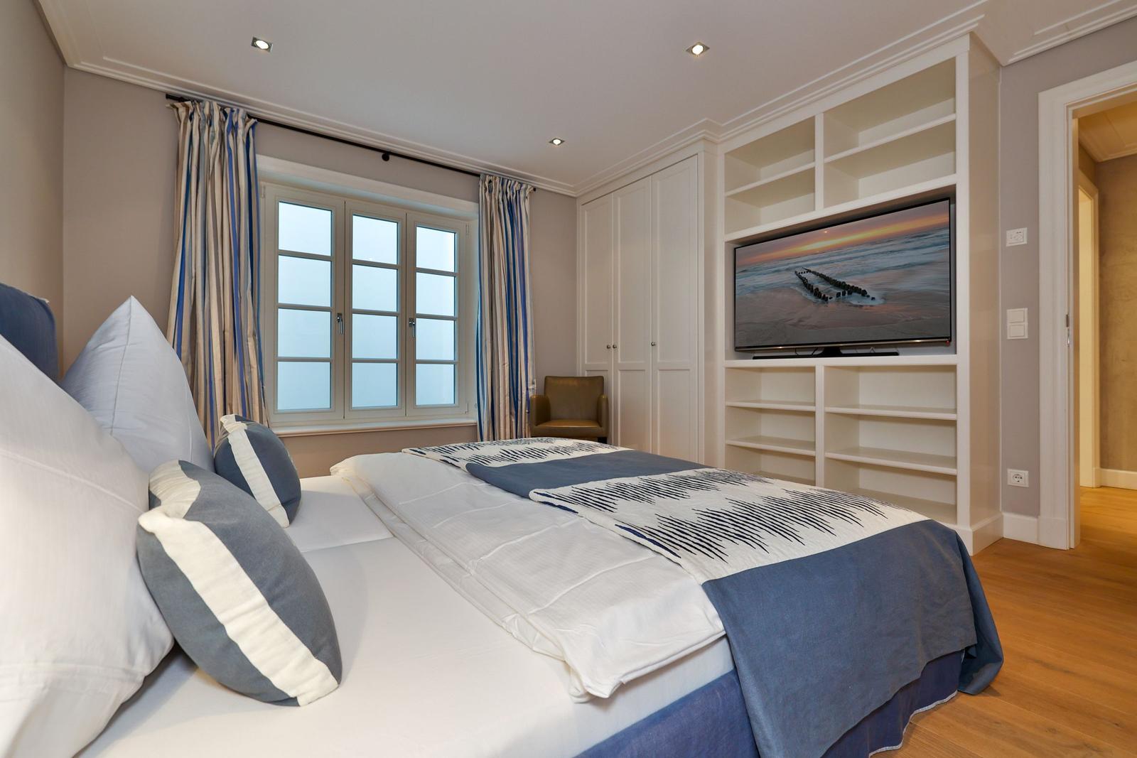 Schlafzimmer mit Bett, TV und Fenster. Holzboden und Einbauschränke.