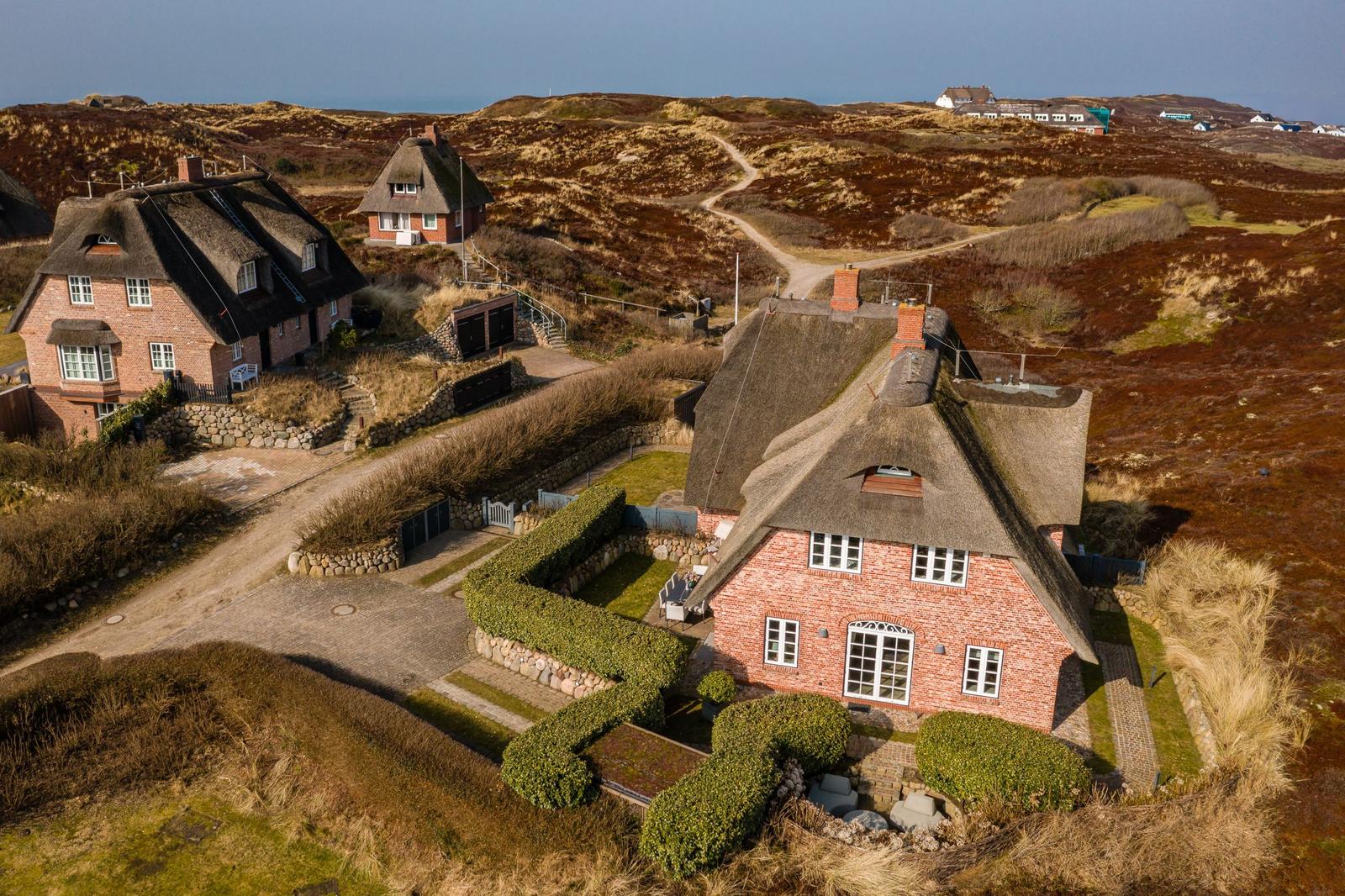 Dachhauses mit Schilfrohren und Steinmauern in hügeligem Gelände.