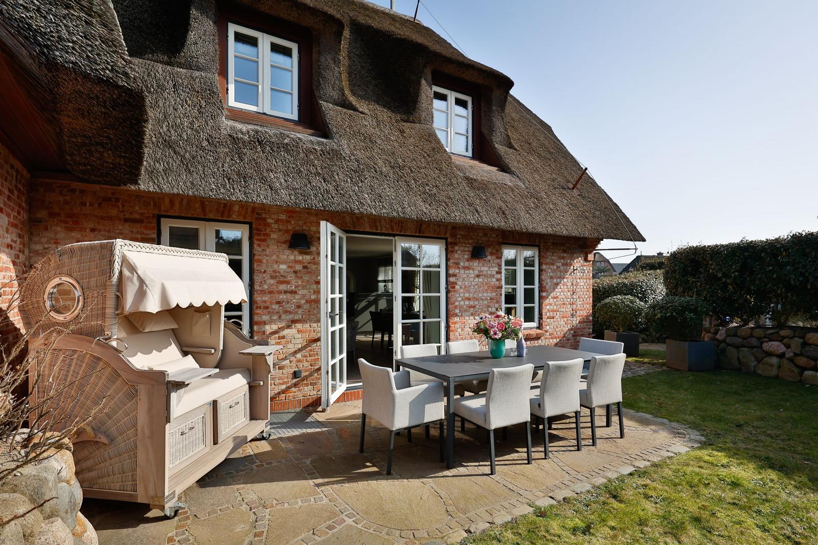 Haus mit Strohdach, Terrasse mit Esstisch und Liegestuhl.