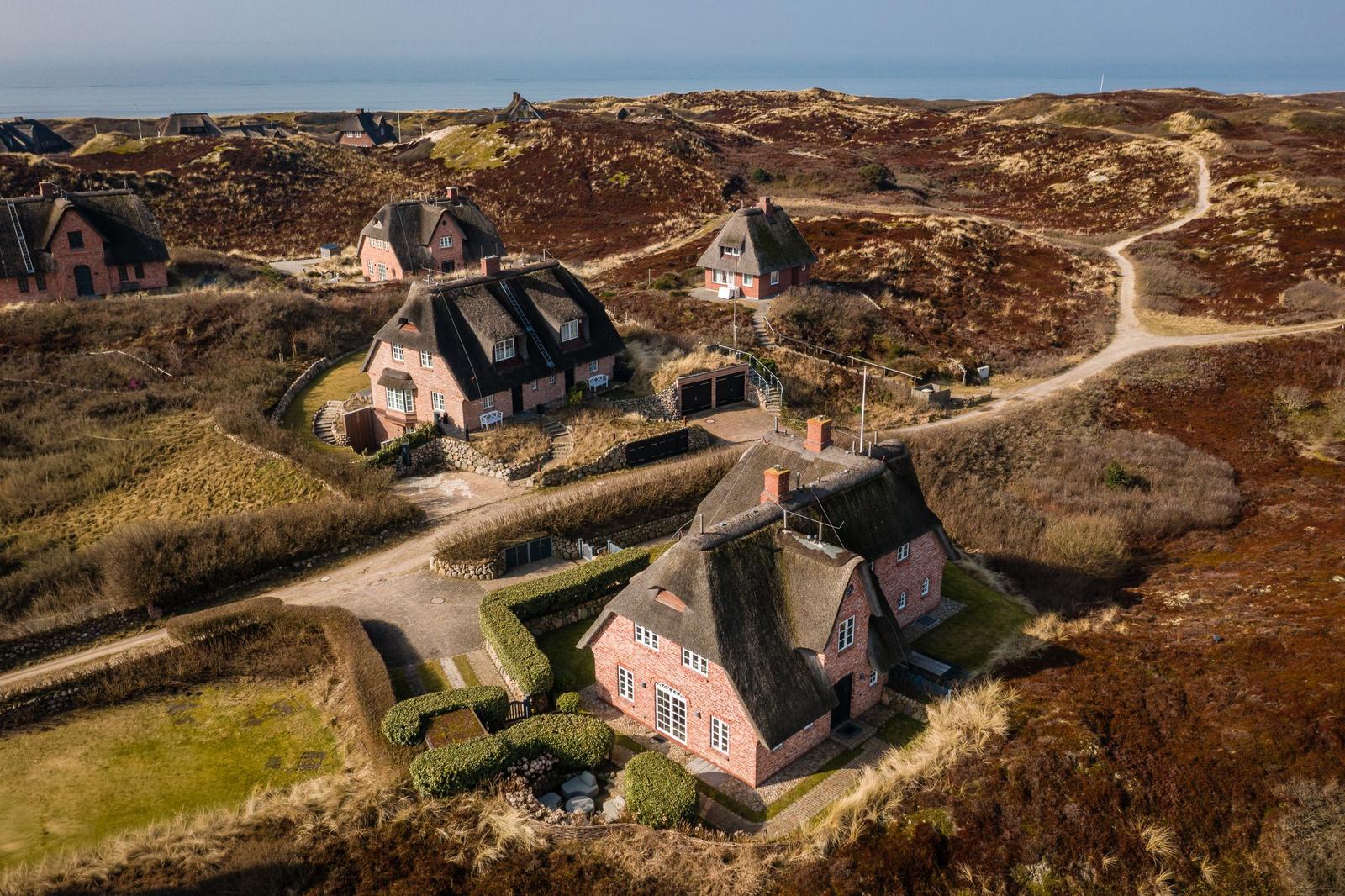 Häuser mit Strohdächern auf einer Dünenlandschaft mit Blick aufs Meer.