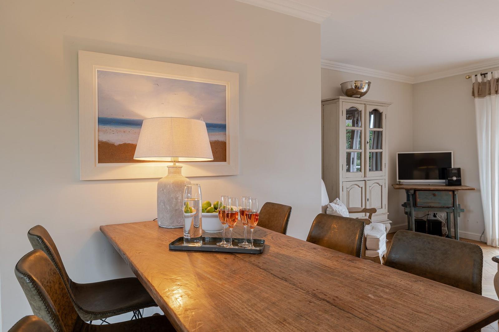 Dining table with chairs, lamp, and picture on the wall. In the background, a cabinet and TV are visible.