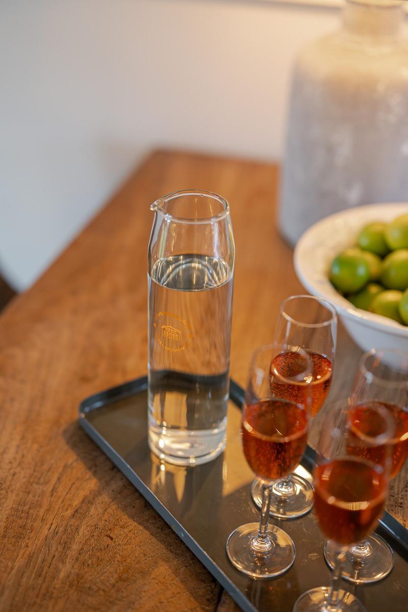 On a wooden table, a water carafe and three glasses with rosé wine.