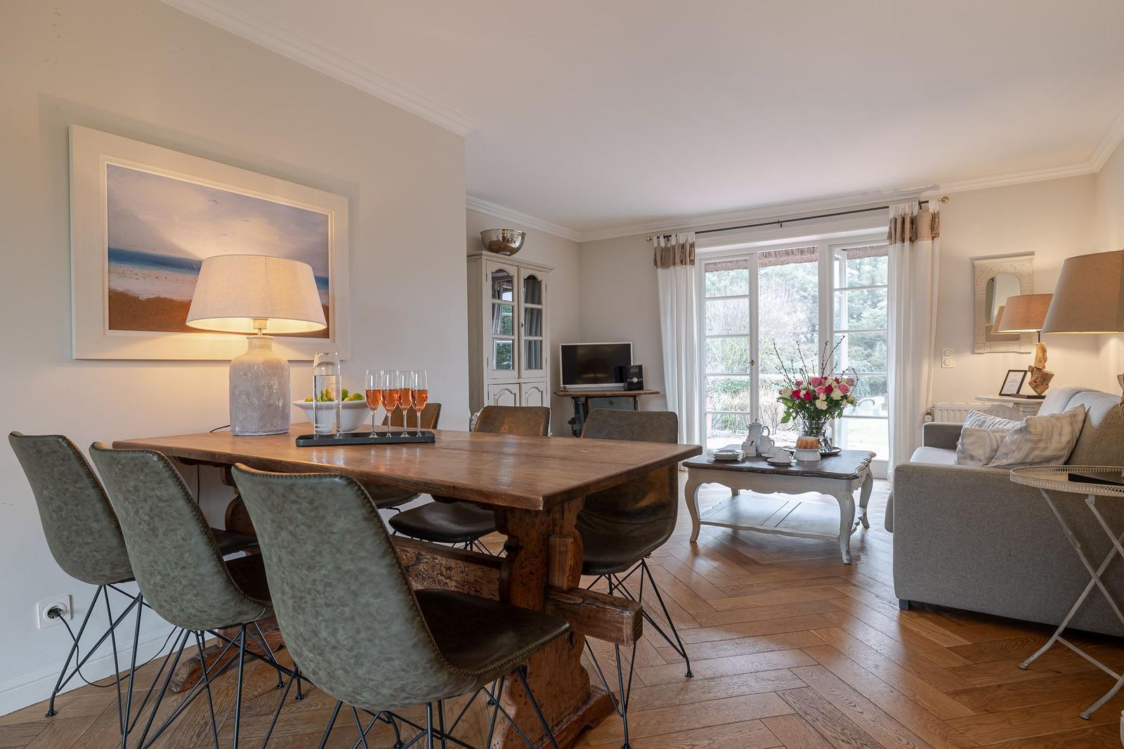 Dining area with wooden table and chairs, living area with sofa and window to outdoor terrace.