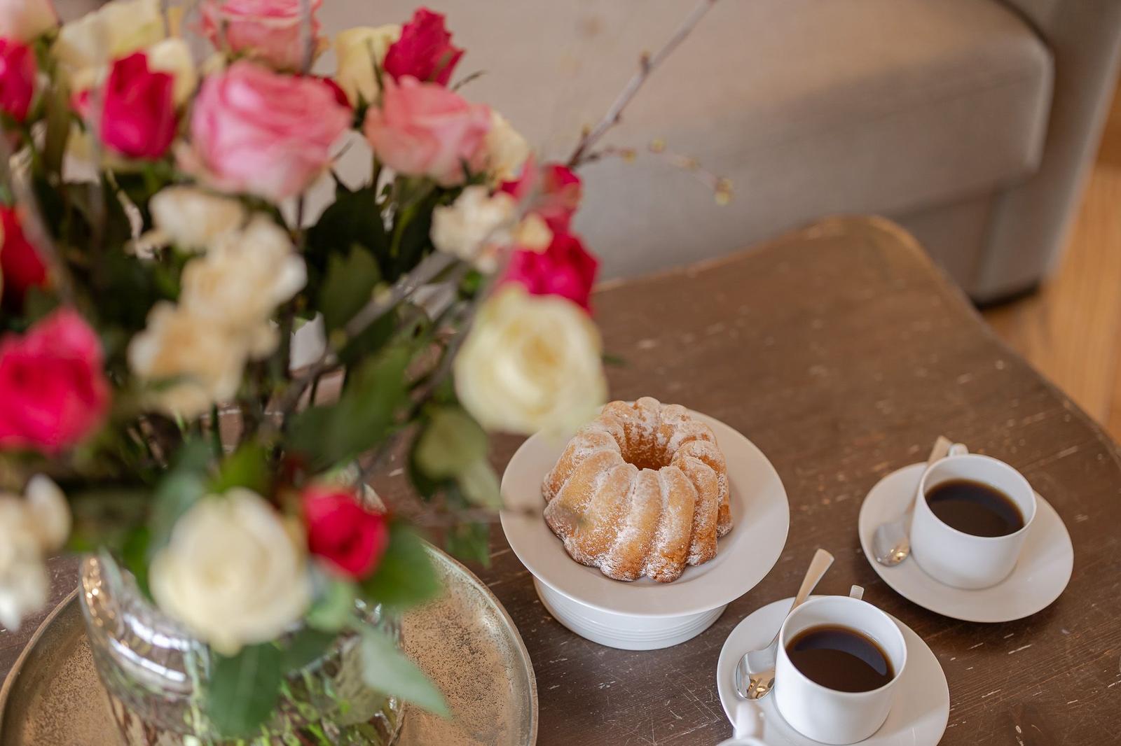 Table with coffee, cake, and floral arrangement.