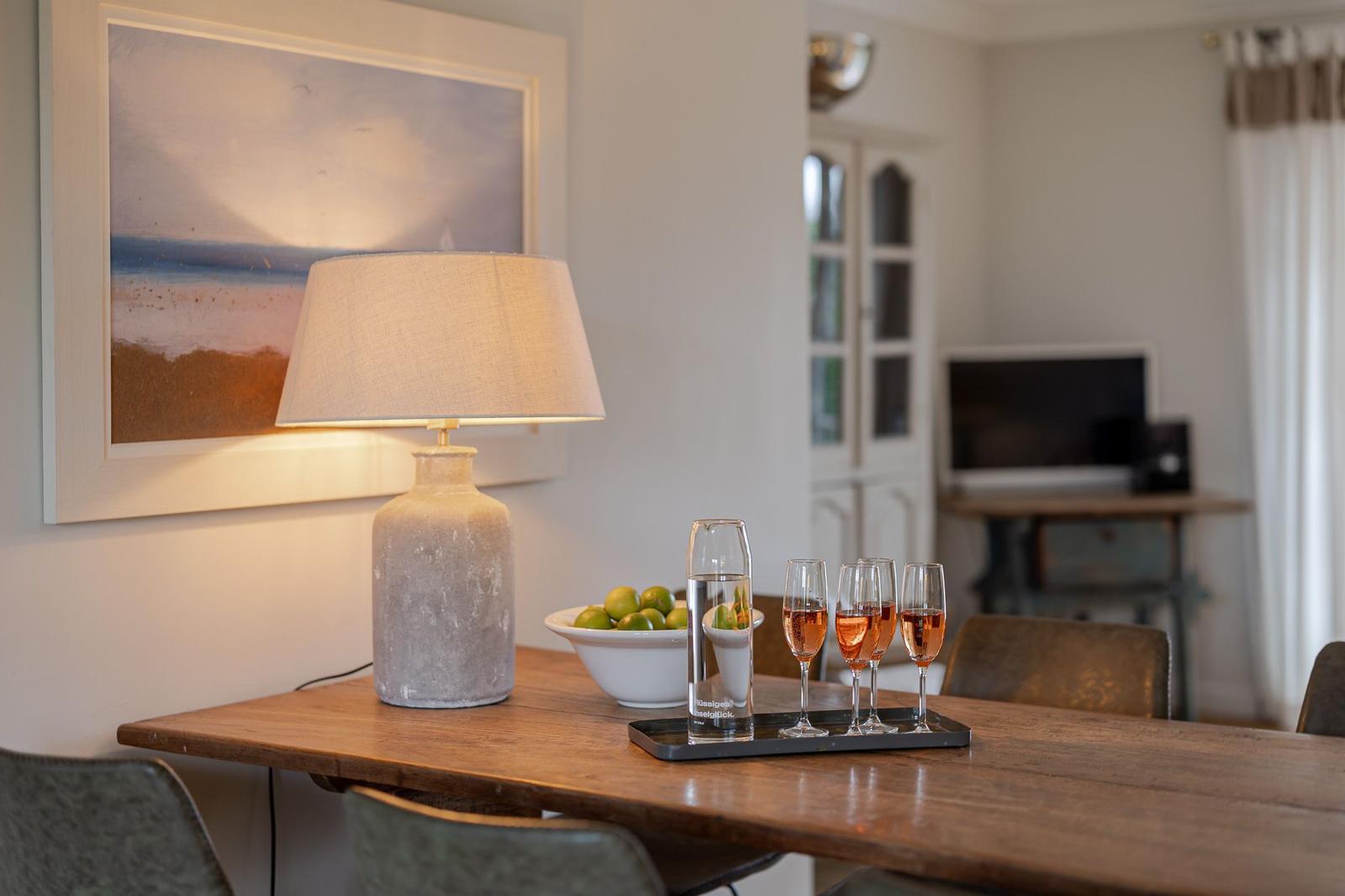 Wooden table with lamp, glasses, and fruit. Wall art and TV in background.