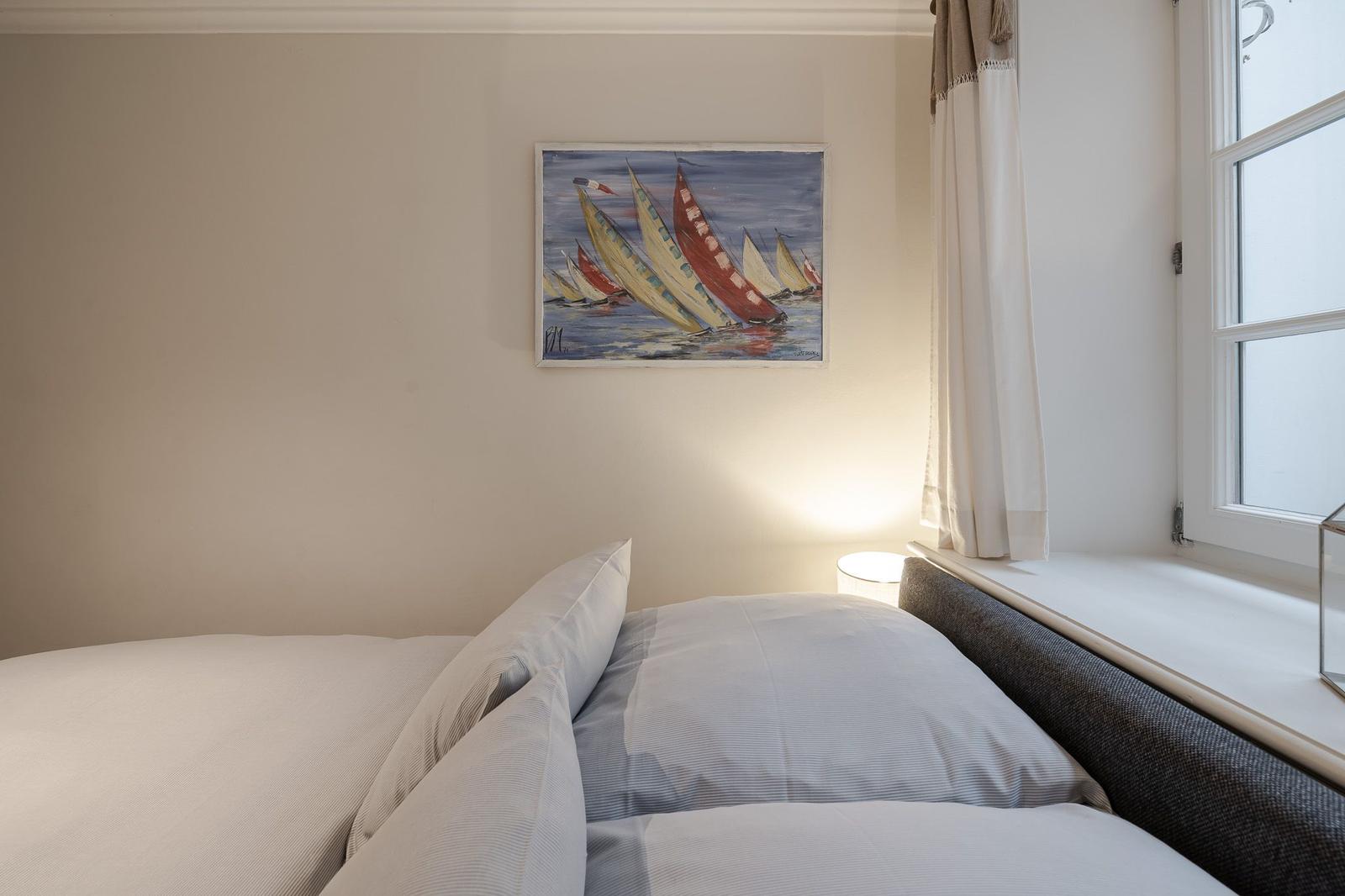 Bedroom with bed, wall painting, and window with curtain.