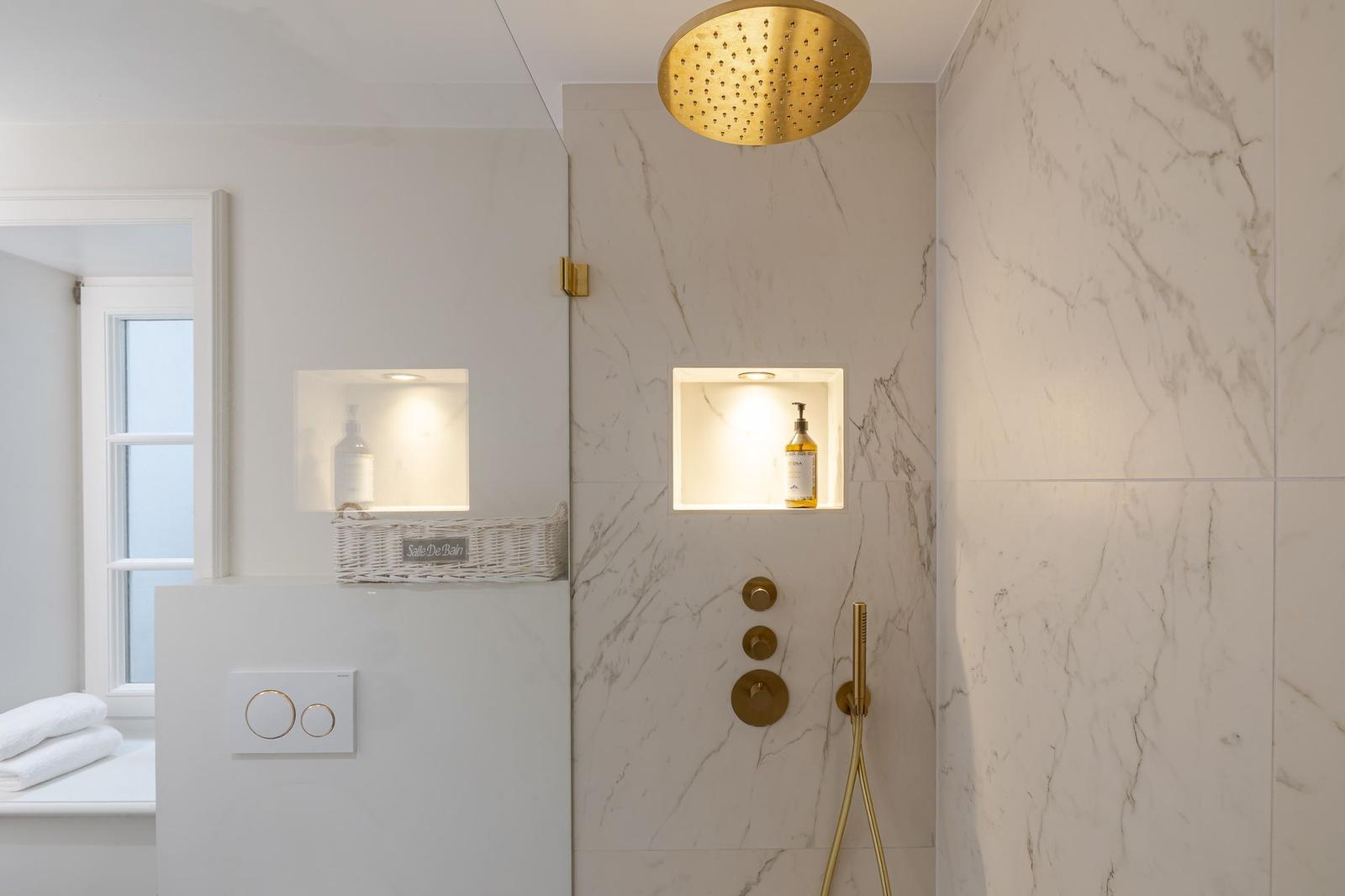 Shower area with gold showerhead and built-in shelves.