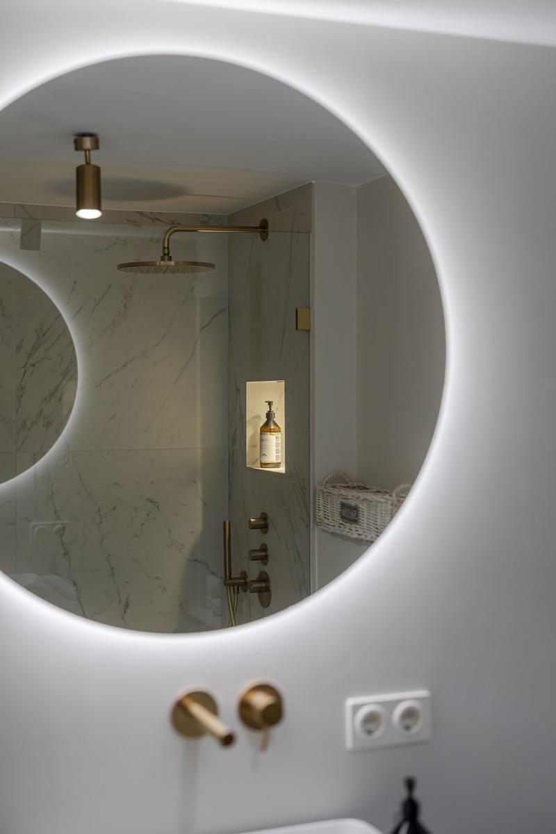 Shower cabin with marble wall and brass fixtures visible through round mirror.