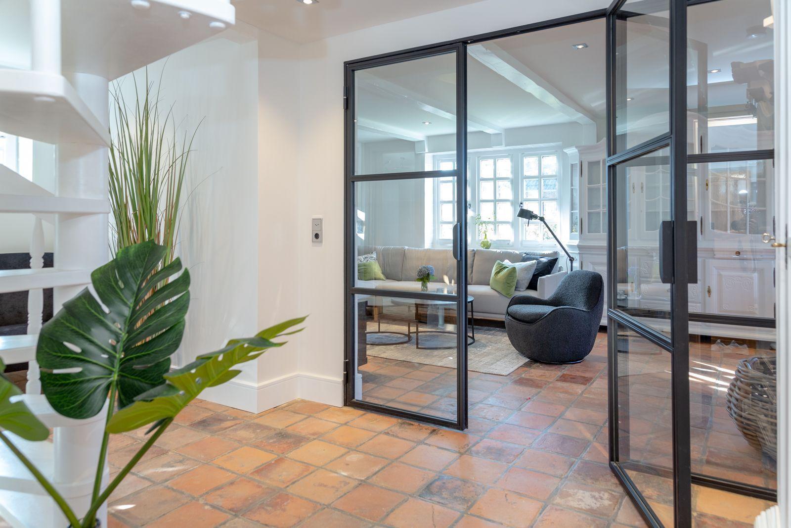 Glass wall separates entrance from living area with sofa and armchair.