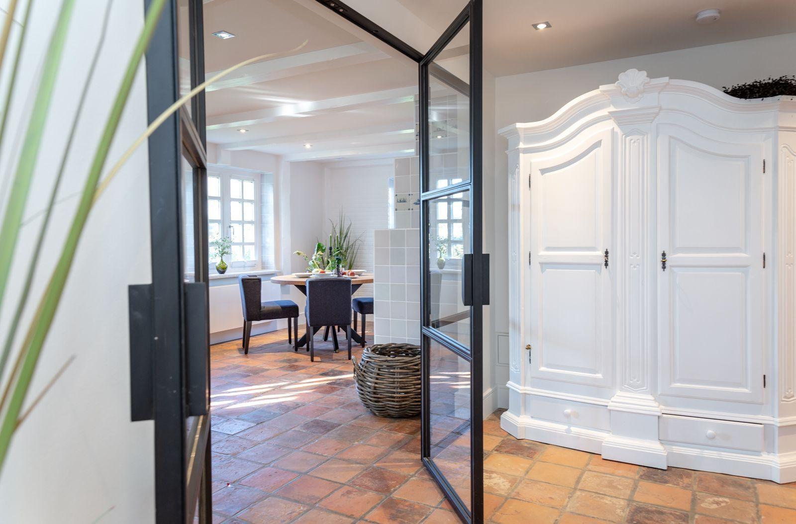 Bright kitchen with dining area and white wardrobe. Terracotta floor and glass walls.