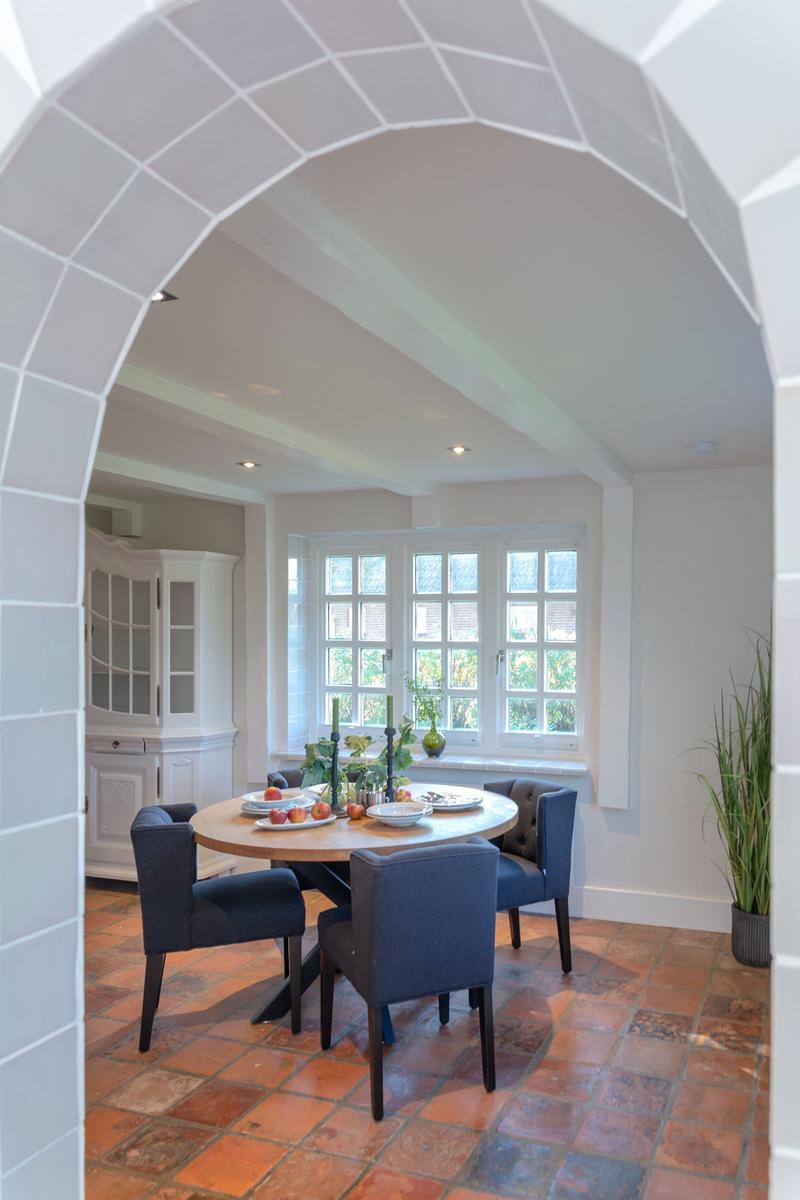 Dining room with round table, blue chairs, and terracotta floor under arched opening.