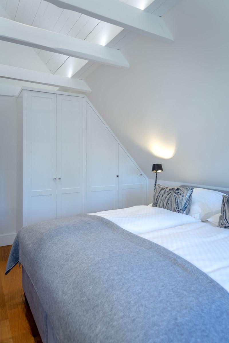 Bedroom with sloped ceiling, white wardrobe, and bed with gray blanket.