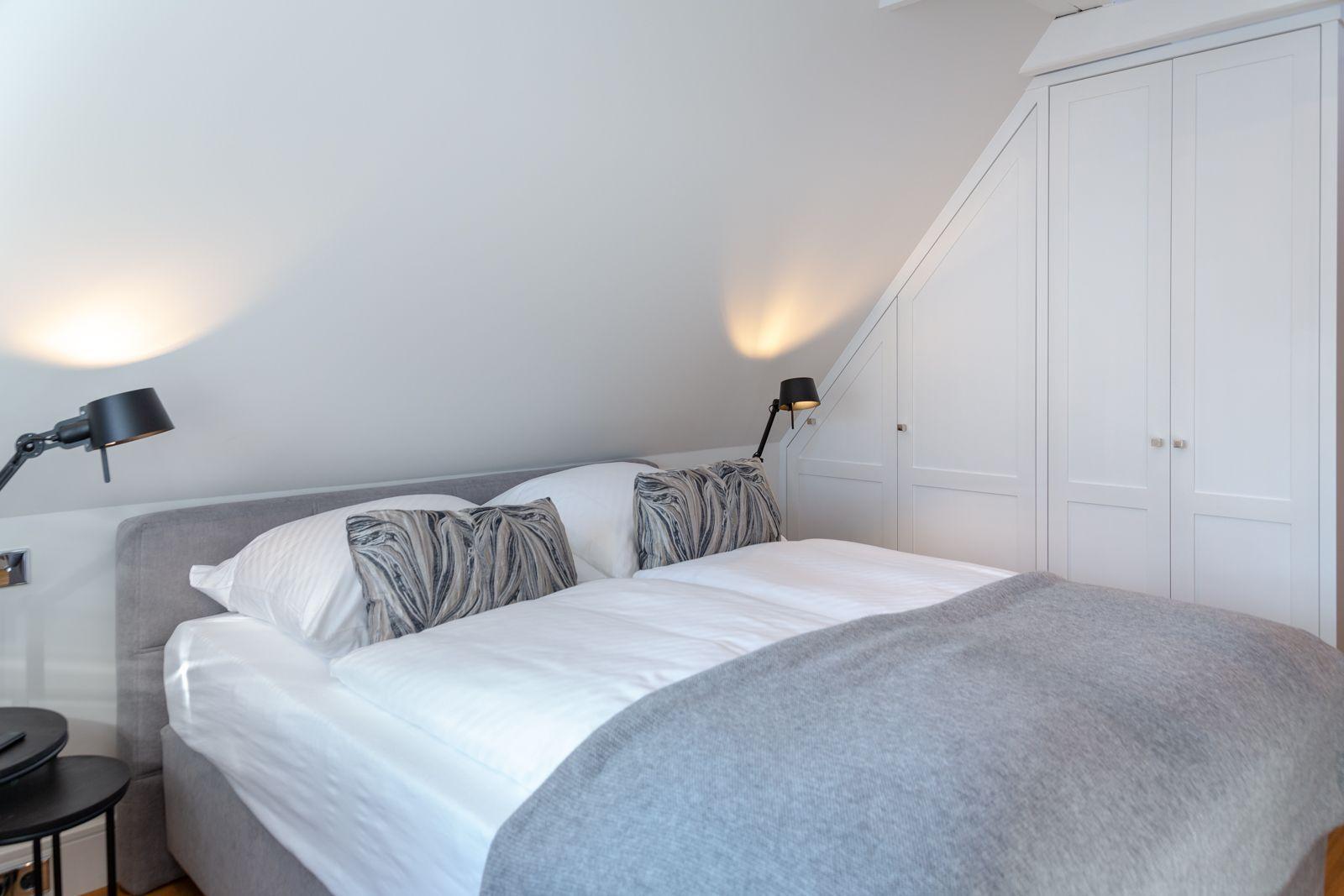 Bedroom with double bed, white walls, and white wardrobes.