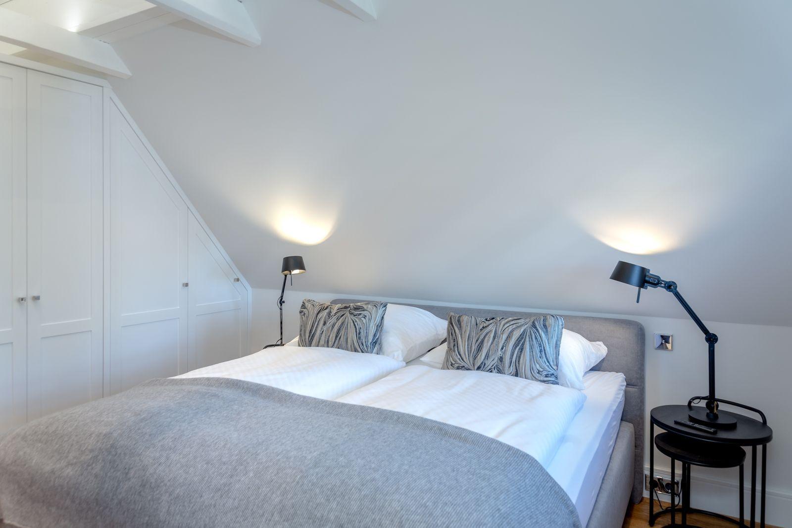 Bedroom with double bed, white walls, and sloped ceiling beams.